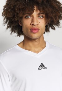 Witte sportshirt met een V-hals ontwerp, gemaakt van gestructureerd fabric. Kenmerkt zich door een zwart Adidas-logo op de borst.