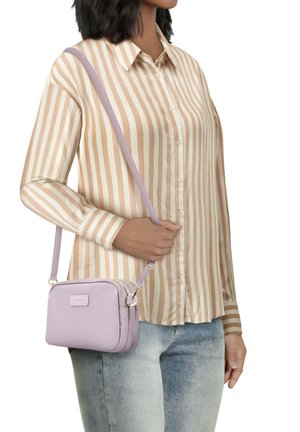 Lilac crossbody bag with a smooth texture, zip closure, and two compartments. Worn on a shoulder strap over a striped shirt.