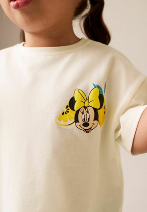 Laps kannab kreemikat särki, mille rinnatükil on Minnie Mouse'i näo graafika, kollane vibu ja sidruniviilud.