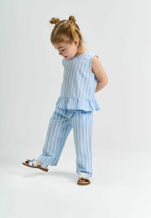 Heled sinine, triibuline t-särk ilma varrukateta, millel on volangäär, koos sobivate lõtvade pükstega. Sandalitel on lilleline aksent. Sujuv kangatekstuur.