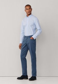 Jasnoniebieska w kratę koszula na guziki, granatowe chinosy i ciemne buty. Koszula ma kołnierzyk; chinosy są slim-fit z kieszeniami.