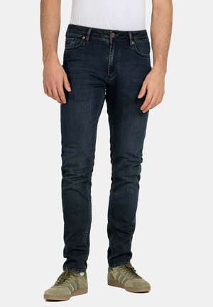 Dunkelblaue Jeans im Slim-Fit. Verfügt über fünf Taschen, einen Knopfverschluss und subtile Stickdetails. Kombiniert mit olivgrünen Sneakers.