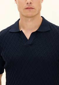Marinblå polo skjorta med diamantmönster, kort ärm och v-ringad krage. Stickad tyg med en mjuk finish.
