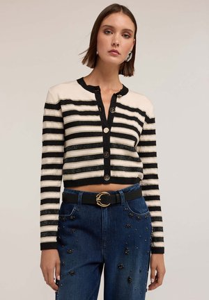 Korte zwarte en witte gestreepte cardigan met een ronde halslijn en knoopsluiting, gecombineerd met donkere jeans met versieringen.