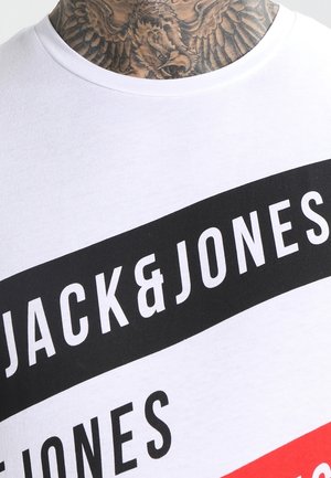 Collo tatuato sopra una maglietta bianca con una striscia diagonale nera e una scritta bianca audace "JACK & JONES" sul petto.