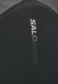 Tecidos pretos texturizados com um acabamento mate, apresentando o logotipo "SALOMON" em letras prateadas contrastantes ao longo de um dos lados.