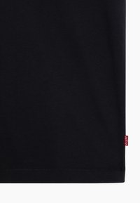 T-shirt en coton noir avec col rond, manches courtes et une petite étiquette rouge Levi's sur l'ourlet. Texture lisse avec un design simple.