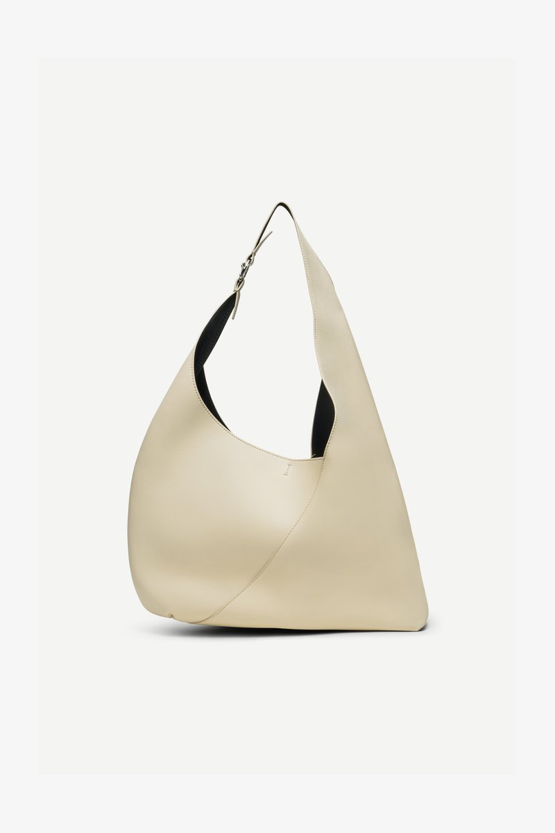 Kreemika värvi sile nahast õlakott, mis on kõveriku kolmnurkse kujuga ja reguleeritava rihmaga, millel on hõbedane pandel.