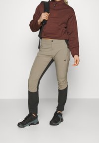 Vinröd tröja med fyrdelad dragkedja, i kombination med beige och svarta taperedbyxor med en logotyp, samt svarta vandringsskor med turkosa detaljer.