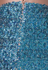 Blå paljettklänning med en texturerad yta. Har en central dragkedja på baksidan, med glänsande, små cirkulära paljetter som reflekterar ljus.