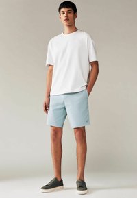 Tricou alb cu mânecă scurtă și pantaloni scurți albaștri deschis dintr-un material neted. Tenisi casual de culoare gri închis. Design simplu, fără ornamente.