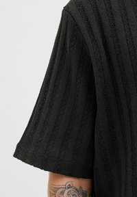 Black knitted top with a textured, ribbed design and short sleeves, featuring subtle openwork accents and a relaxed fit.