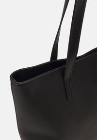 Črna torba tote iz gladke usnjene strukture z dvema trdnima ročajema, ki se ponaša z čistim, minimalističnim dizajnom in odprtim zgornjim delom za enostaven dostop.