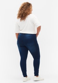 Vaqueros skinny de mezclilla azul oscuro con cintura alta, con bolsillos traseros y una textura suave. Combinados con una camiseta blanca de manga corta.