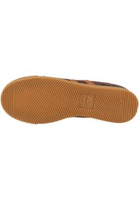 Suola di sneaker caratterizzata da un motivo a spina di pesce, materiale in gomma, colori marrone e arancione, con un logo stampato al centro.