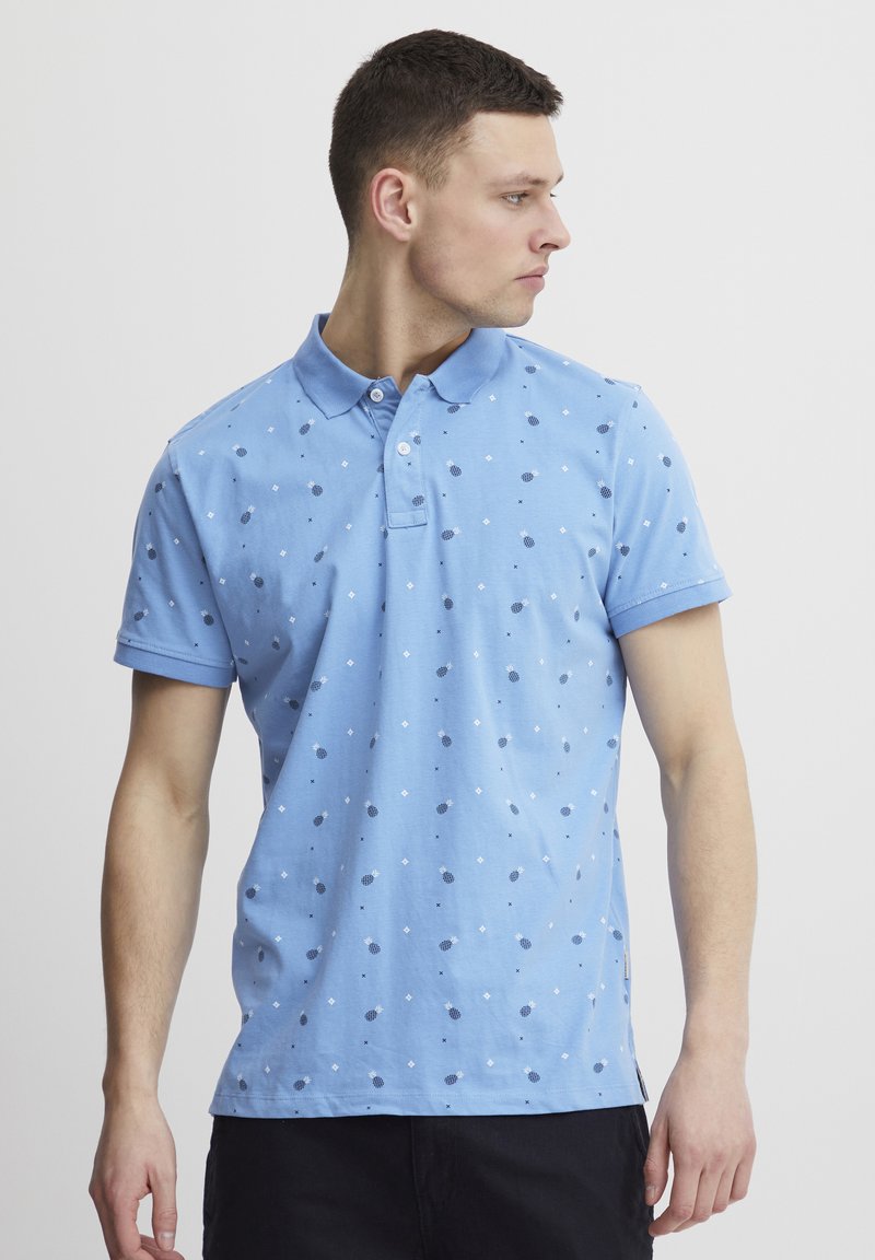 Lyseblå poloshirt laget av bomull, med et spredt mønster av mørkeblå prikker og diamanter, med krage og korte ermer.