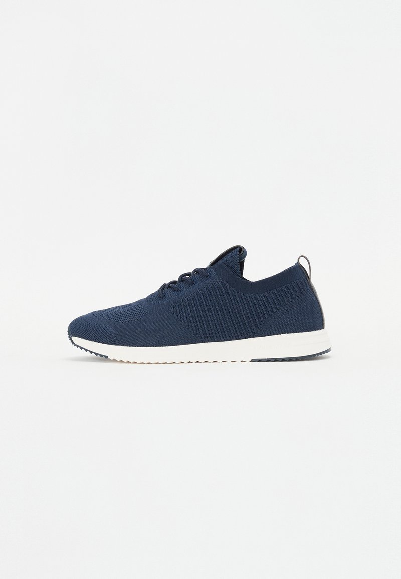 Navy blue athletic shoe with a knitted upper featuring textured patterns. White sole with a slight heel and a pull tab at the back.