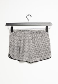 Pantalones cortos gris claro con un patrón de lunares, cintura elástica y ribete negro en contraste, colgando de una percha de metal negro.