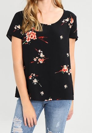 Zwarte blouse met korte mouwen en roze en witte bloemenprint, gedragen met lichtblauwe gescheurde spijkerbroek.