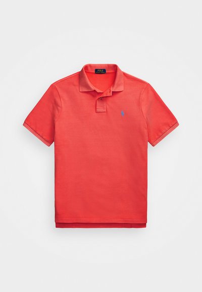 Sarkans polo krekls no kokvilnas, ar klasisku apkakli, īsām piedurknēm un mazu zilu logo kreisajā krūtī. Gluda tekstūra.