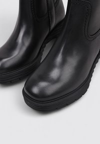 Bottines noires en cuir avec un bout arrondi, une surface texturée et des semelles en caoutchouc. Présentent des coutures discrètes sur les côtés.