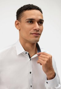 Chemise blanche avec un col en marine contrastant et des boutons. Tissu lisse, coupe ajustée, avec un col classique et des poignets à boutons.