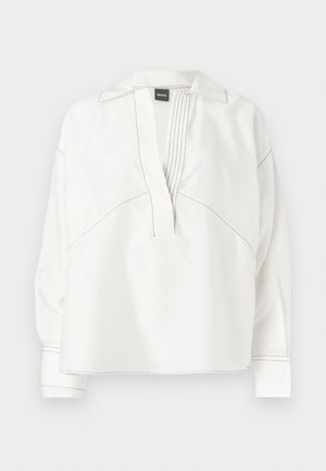 White blouse with a collared neckline, pleated front detail, and contrasting black stitching. Features long sleeves and a relaxed fit.