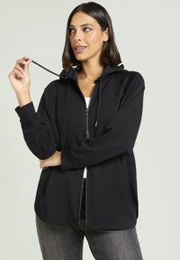 Felpa nera con zip e cappuccio regolabile, realizzata in tessuto morbido. Presenta maniche lunghe, tasche laterali e una vestibilità comoda.