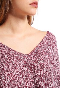 V-Ausschnitt Strickpullover in Rot und Weiß, mit strukturiertem Muster und lockerem Schnitt, mit ausgefransten Kanten am Ausschnitt.