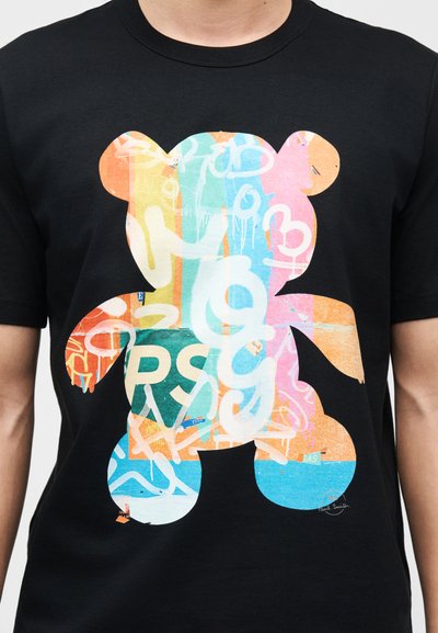 Μαύρο μπλουζάκι με μεγάλο πολύχρωμο σχέδιο αρκουδάκι, που διαθέτει αφηρημένα μοτίβα σε στυλ γκράφιτι και γράμματα στο μπροστινό μέρος.