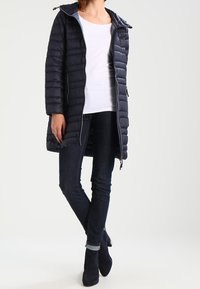 Navy Pufferjacke mit hohem Kragen, Reißverschlussfront und Seitentaschen. Kombiniert mit dunklen Jeans und Ankle Boots, die einen lässigen Winterlook betonen.