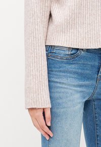 Pull en tricot rose clair à manches longues, associé à un jean en denim bleu délavé. Texture douce et coupe décontractée à la taille.