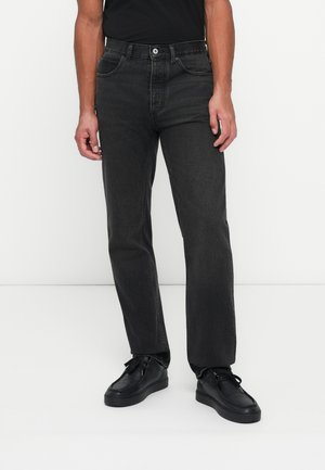 Vaqueros de mezclilla negra con un diseño de pierna recta, estilo de cinco bolsillos y decoloración sutil. Combinados con zapatos negros y una camiseta ajustada negra.