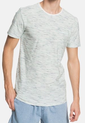 Homme portant un t-shirt à manches courtes gris clair chiné et un short en denim bleu clair, debout devant un fond blanc.