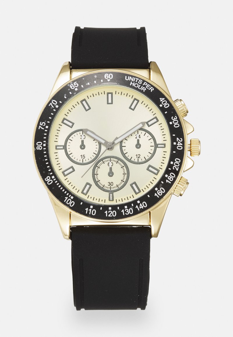 Montre chronographe dorée avec une lunette noire, un cadran crème, trois sous-cadrans et un bracelet en silicone noir. Présente des repères de minutes et des poussoirs.