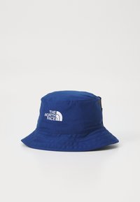 Blå bucketskap med bred brätte, broderad vit logga på framsidan och en texturerad ytfinish.