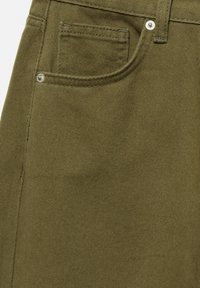 Gros plan sur un pantalon en denim vert olive montrant la poche avant, des rivets métalliques, une boucle de ceinture et des coutures détaillées.