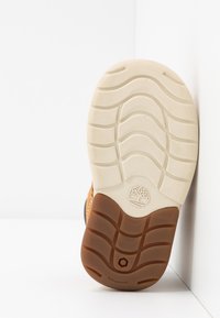 Brown rubber shoe sole with a wavy tread pattern, featuring a white midsole and a logo imprint. Durable, non-marking design.