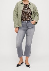 Olivgrön jacka med krage över en leopardmönstrad topp; ljusgrå beskurna jeans och svarta slingbackskor med silverdetaljer.