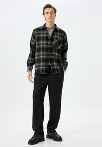 Camicia a quadri bianca e nera con bottoni, design con colletto. Indossata sopra una maglia grigia, abbinata a pantaloni neri larghi e stivali neri.