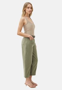 Top in cotone beige aderente e pantaloni larghi in cotone verde oliva con tasche laterali, una cintura e taglio dritto, indossati con sandali minimalisti.