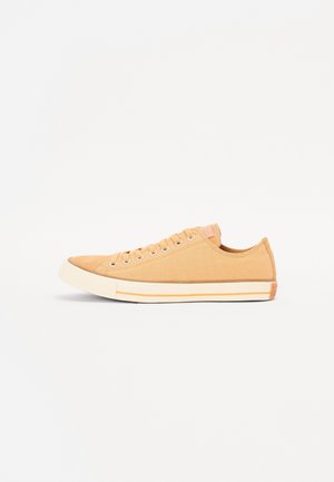 Zapatillas de lona color camel con punta redondeada, seis ojales, suela de goma y rayas contrastantes en blanco y naranja a lo largo del borde.