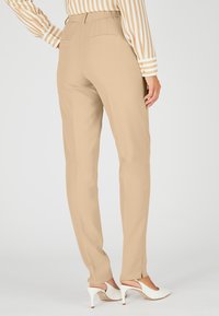 Beige op maat gemaakte broek met een rechte pijp ontwerp, subtiele plooien en twee achterzakken, gecombineerd met witte hoge hakken.
