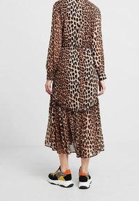 Leopardenmuster-Kleid mit langen Ärmeln, gestuftem Saum und elastischem Bund, kombiniert mit schwarzen und orangefarbenen Turnschuhen. Halbtransparenter Stoff.