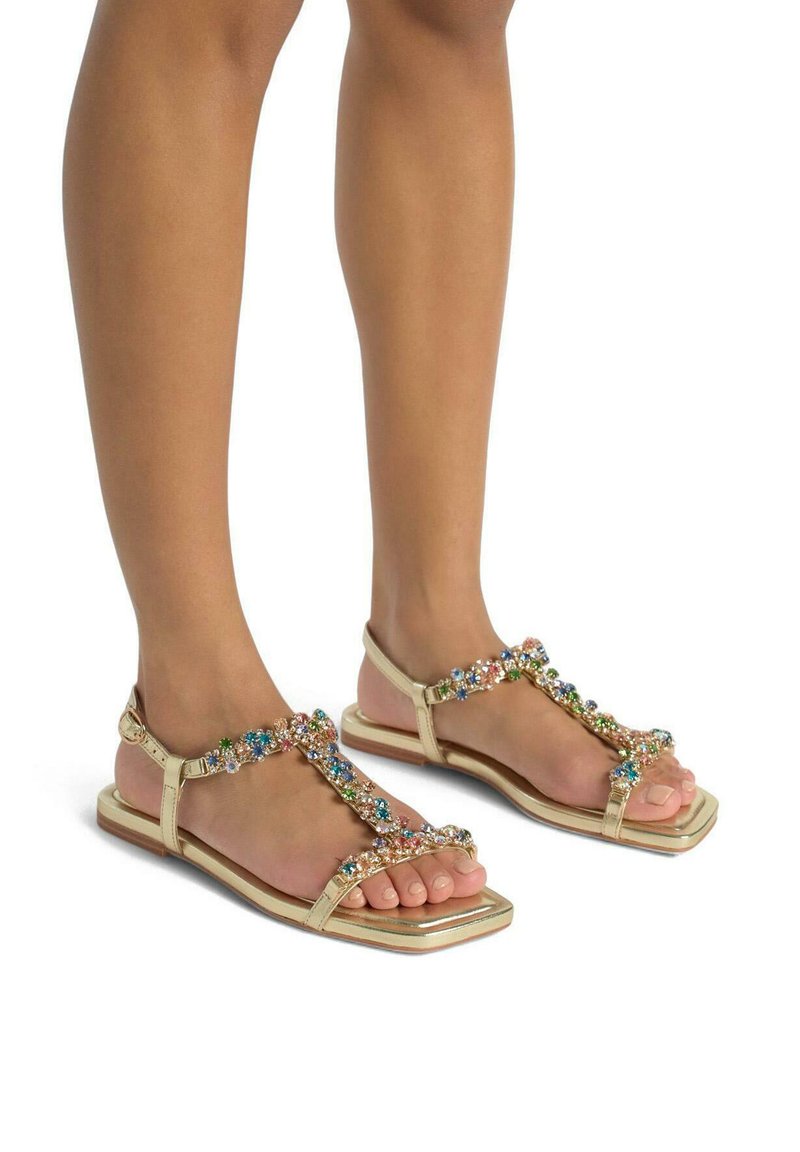 Sandales plates dorées avec un design à tige en T, ornées de pierres précieuses multicolores, bout carré et semelle plate marron.