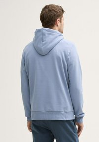 Hanorac din bumbac de culoare albastră deschisă, cu glugă, manșete și talie ribbate, având o textură netedă și un design minimalist.