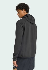 Hoodie noir au toucher lisse, avec une capuche ajustée, des manches longues et des coutures contrastées le long des seams.