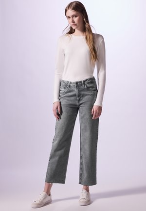 Jeans grises de tiro alto con pierna recta y dobladillo deshilachado, combinados con una camiseta blanca de manga larga y zapatillas blancas. Textura de tela suave.