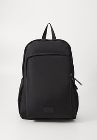 Sort nylon rygsæk med en glat tekstur, en frontlomme med lynlås, sideadgang og justerbare stropper. Udstyret med et logo-patch på bunden.