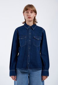 Dunkelblaue Jeanshemd mit langen Ärmeln, durchgehender Knopfleiste, zwei Brusttaschen und Kontrastnähten. Weicher Stoff und entspannter Schnitt.
